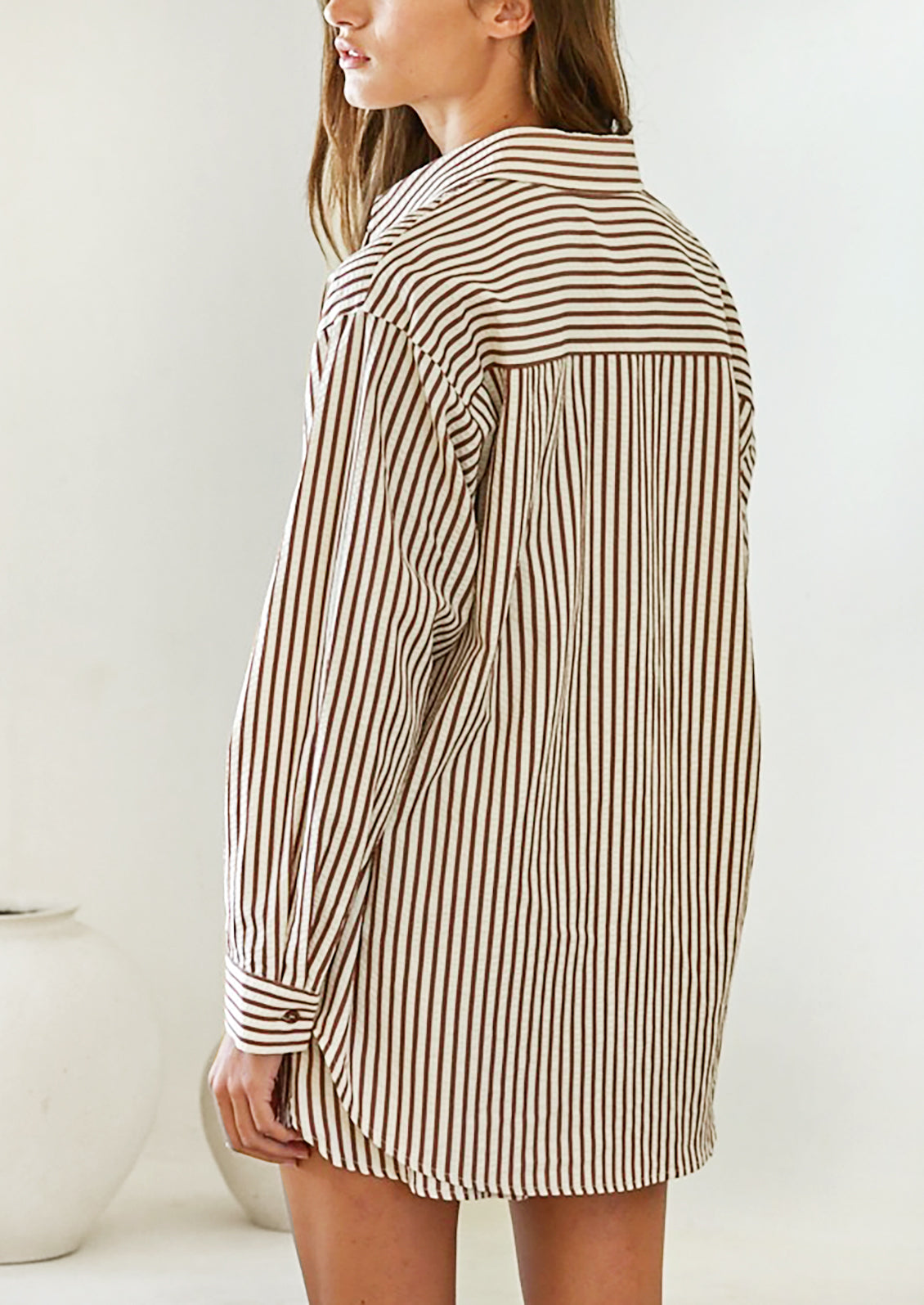 A woman wearing a long sleeve button front shirt in white with brown stripes.
