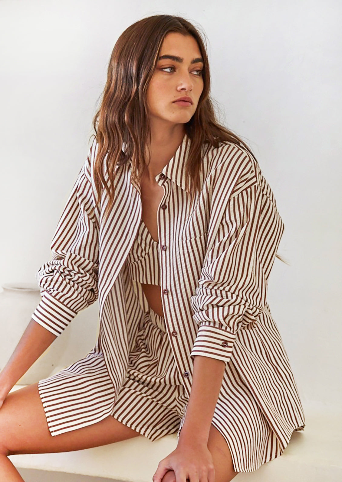 A woman wearing a long sleeve button front shirt in white with brown stripes.