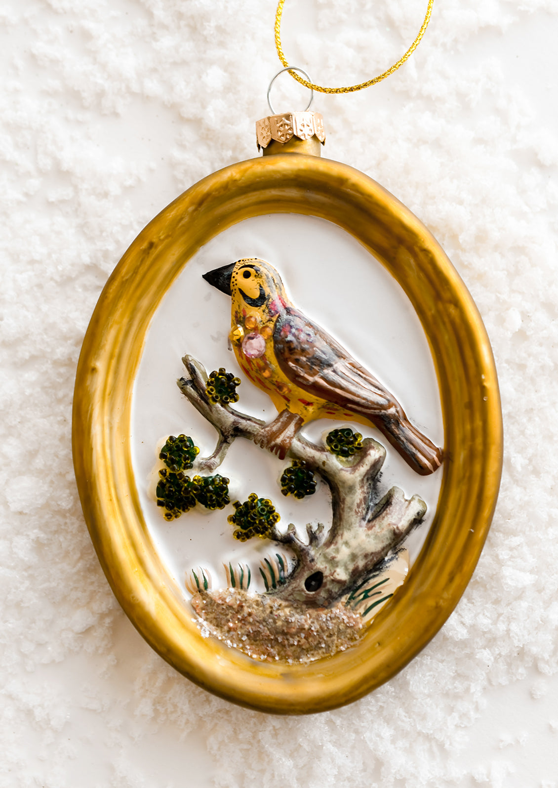 A glass ornament of gold frame around yellow bird.