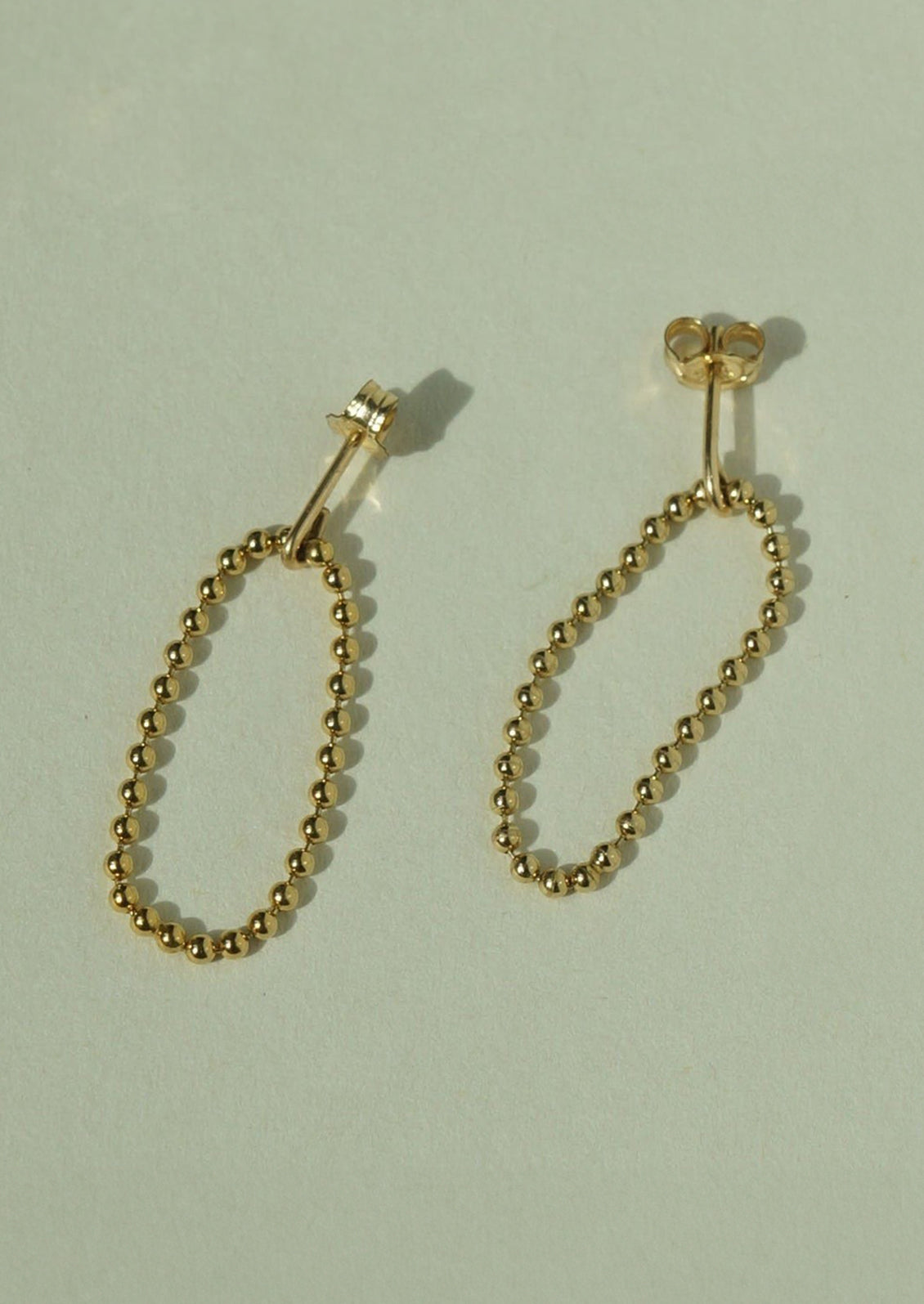 A pair of gold post back earrings with ball chain loop front.