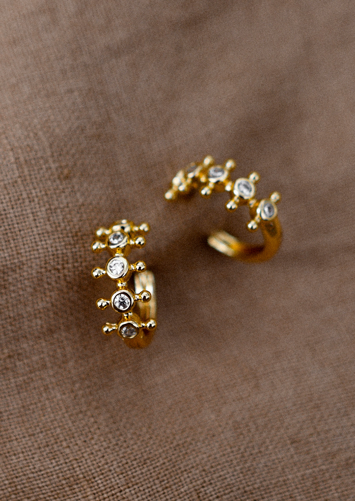 A pair of gold huggie hoop earrings with bezeled clear crystals and decorative ball flange.