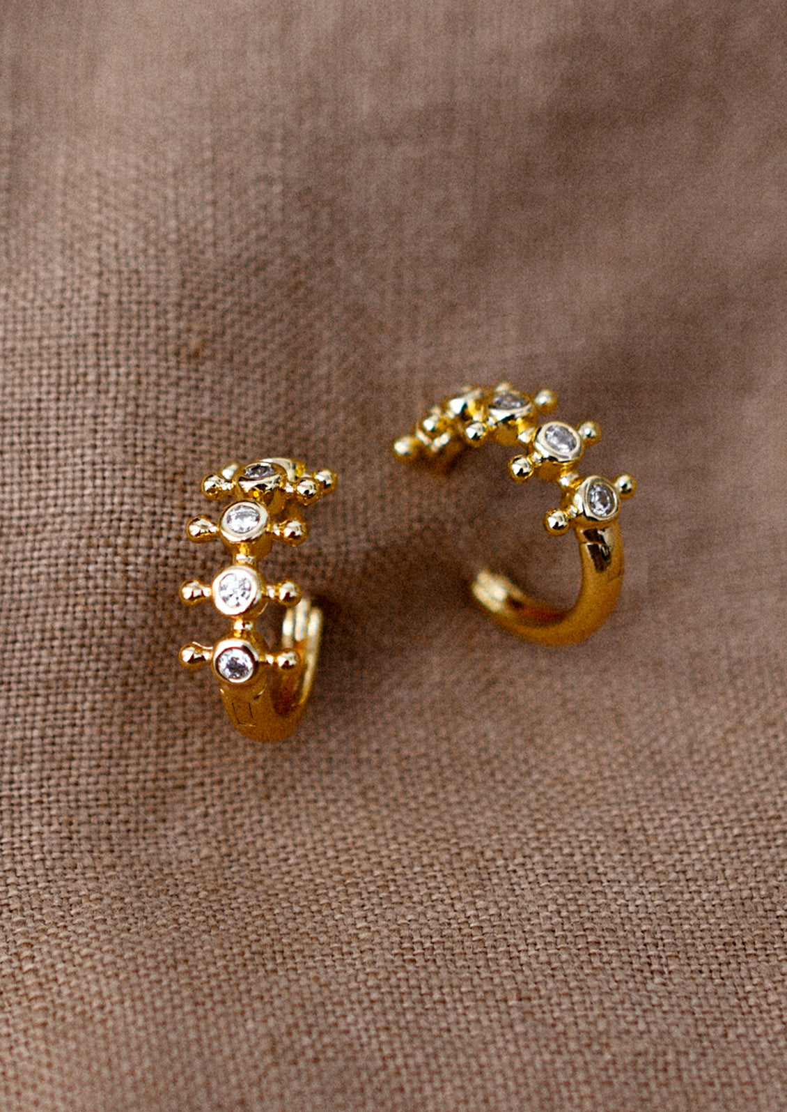 A pair of gold huggie hoop earrings with bezeled clear crystals and decorative ball flange.