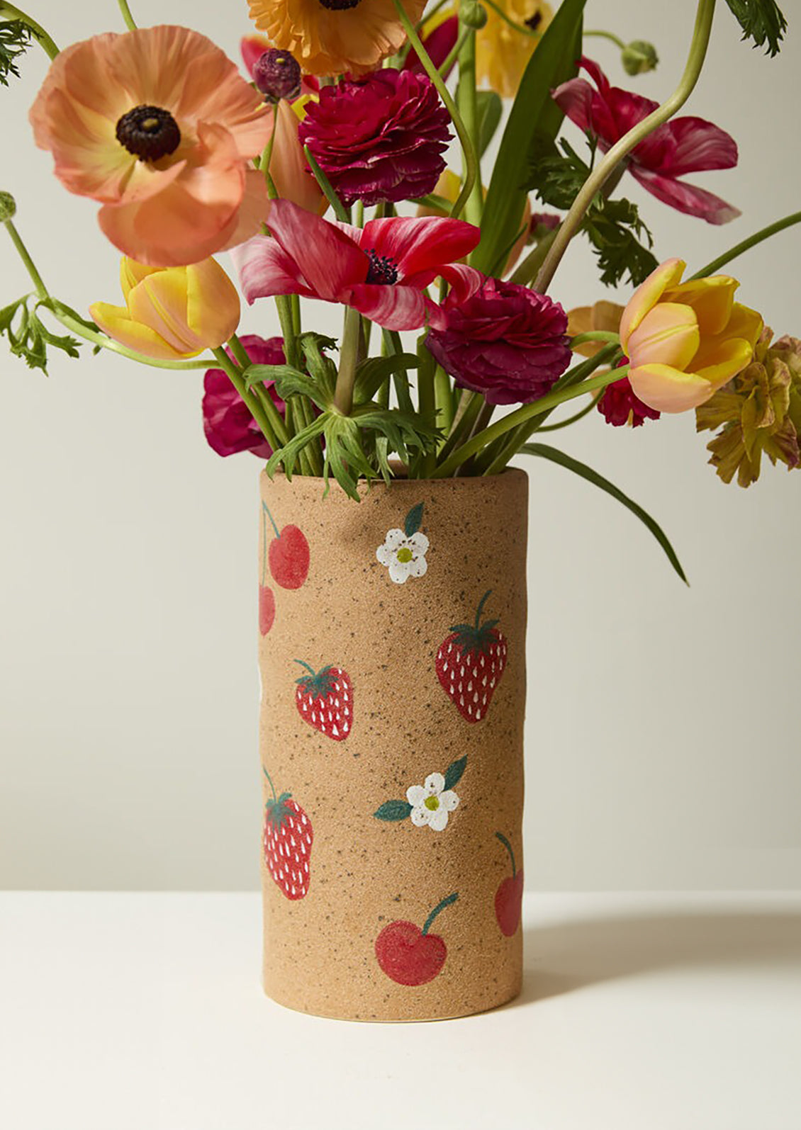 A sandy ceramic vase with painted berry pattern.