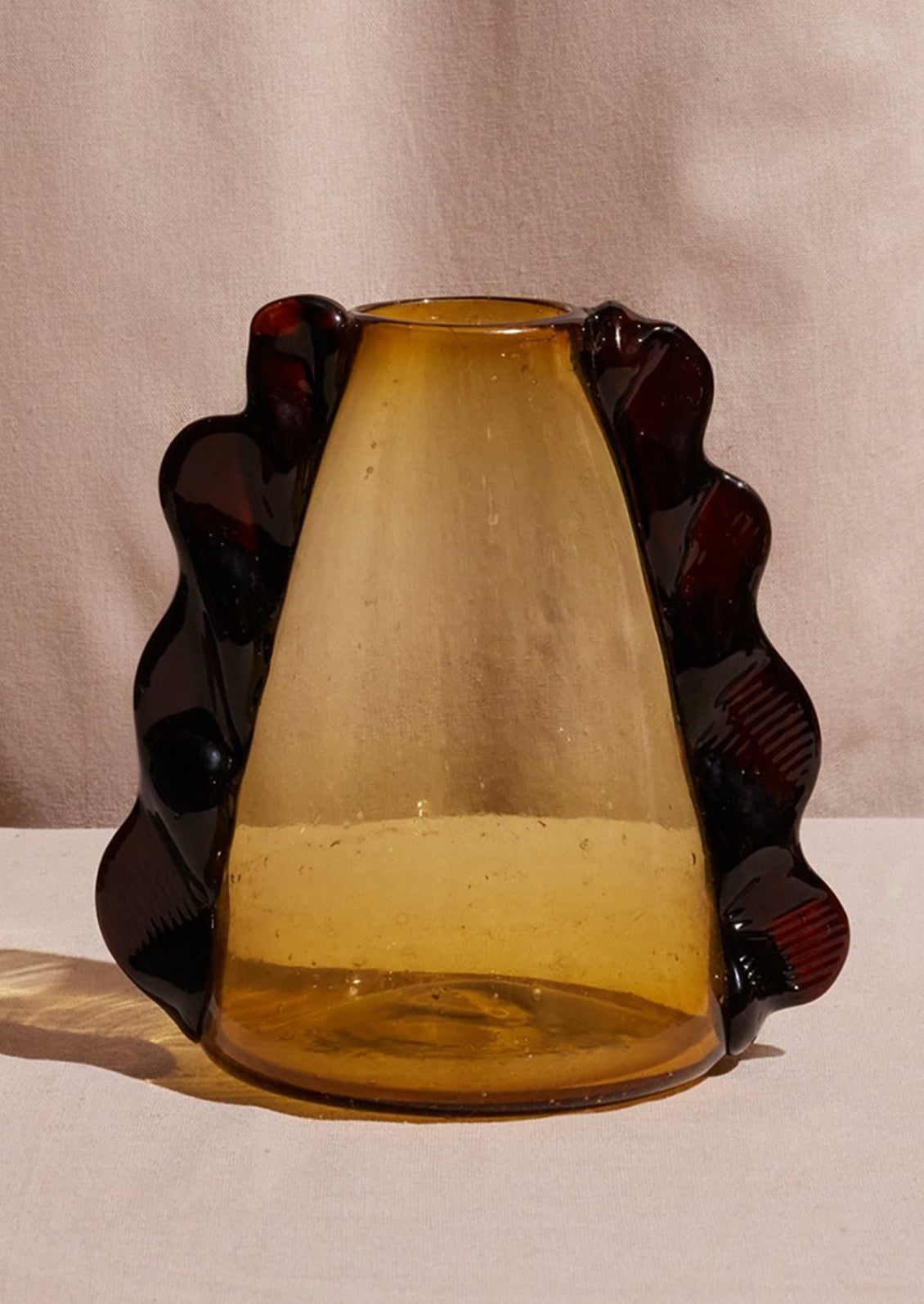 A recycled glass vase with amber hue, wavy "handles" on sides.