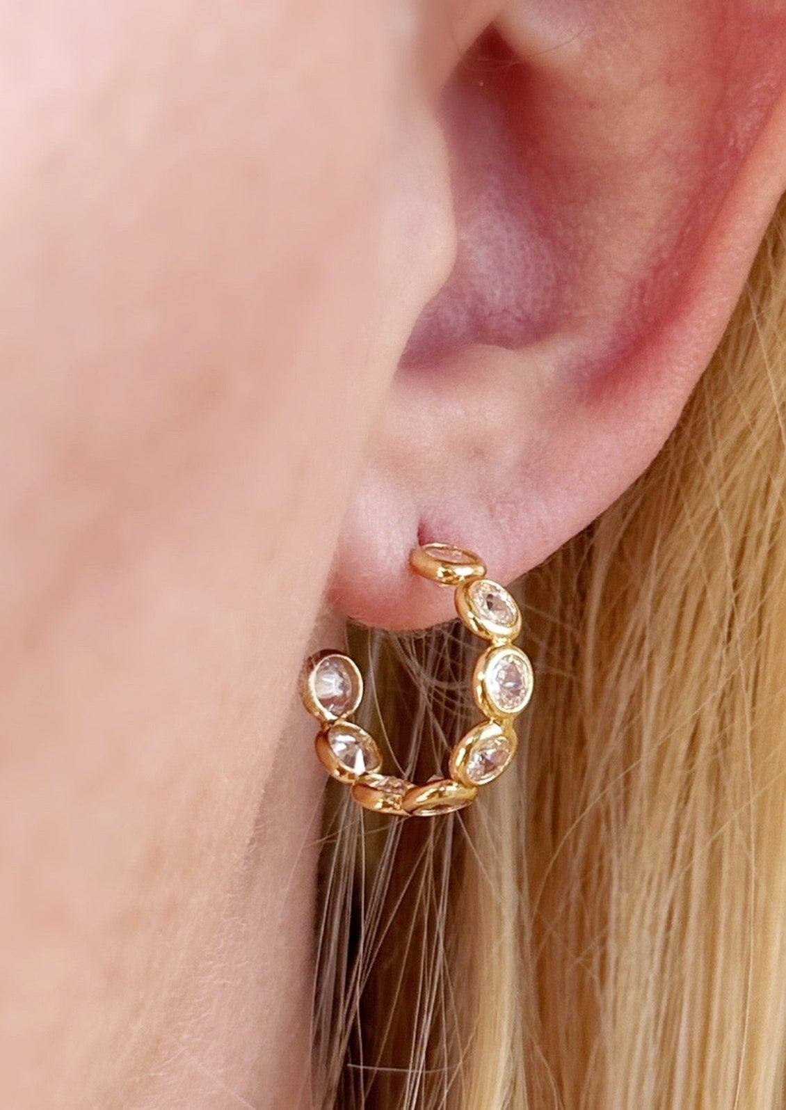 A pair of gold hoop earrings with clear bezeled circles.