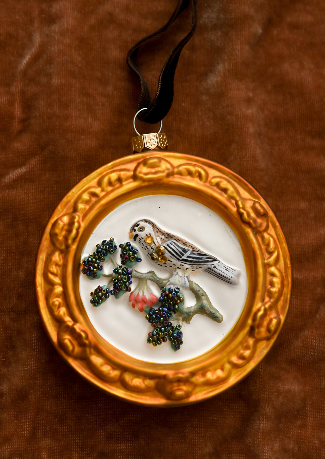 A circular glass ornament with sparrow bird on branch inside gold frame.