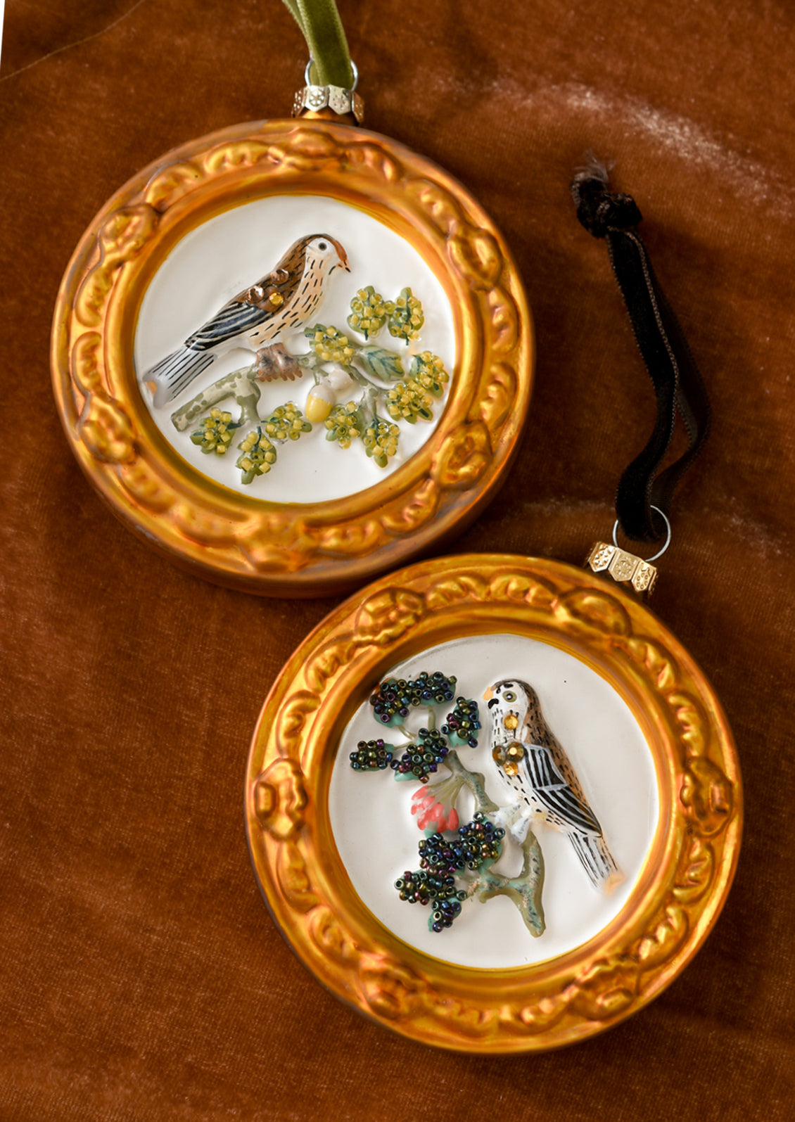 Glass ornaments of birds on a branch with round gold frames.