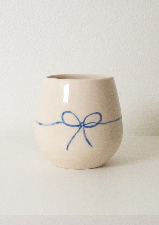 A white rounded ceramic cup with hand painted blue bow.