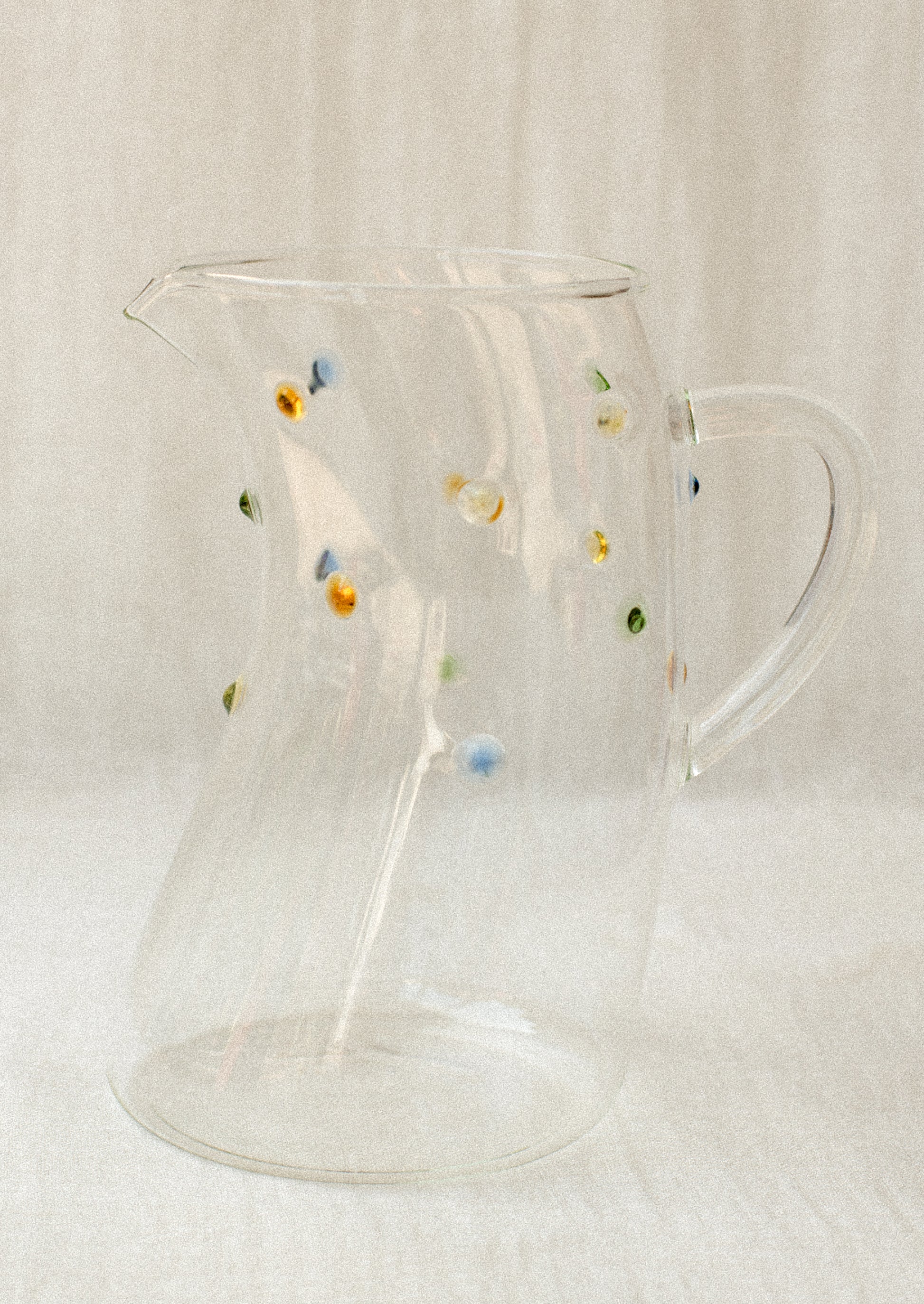 A skewed shape clear glass pitcher with colorful dot detail.