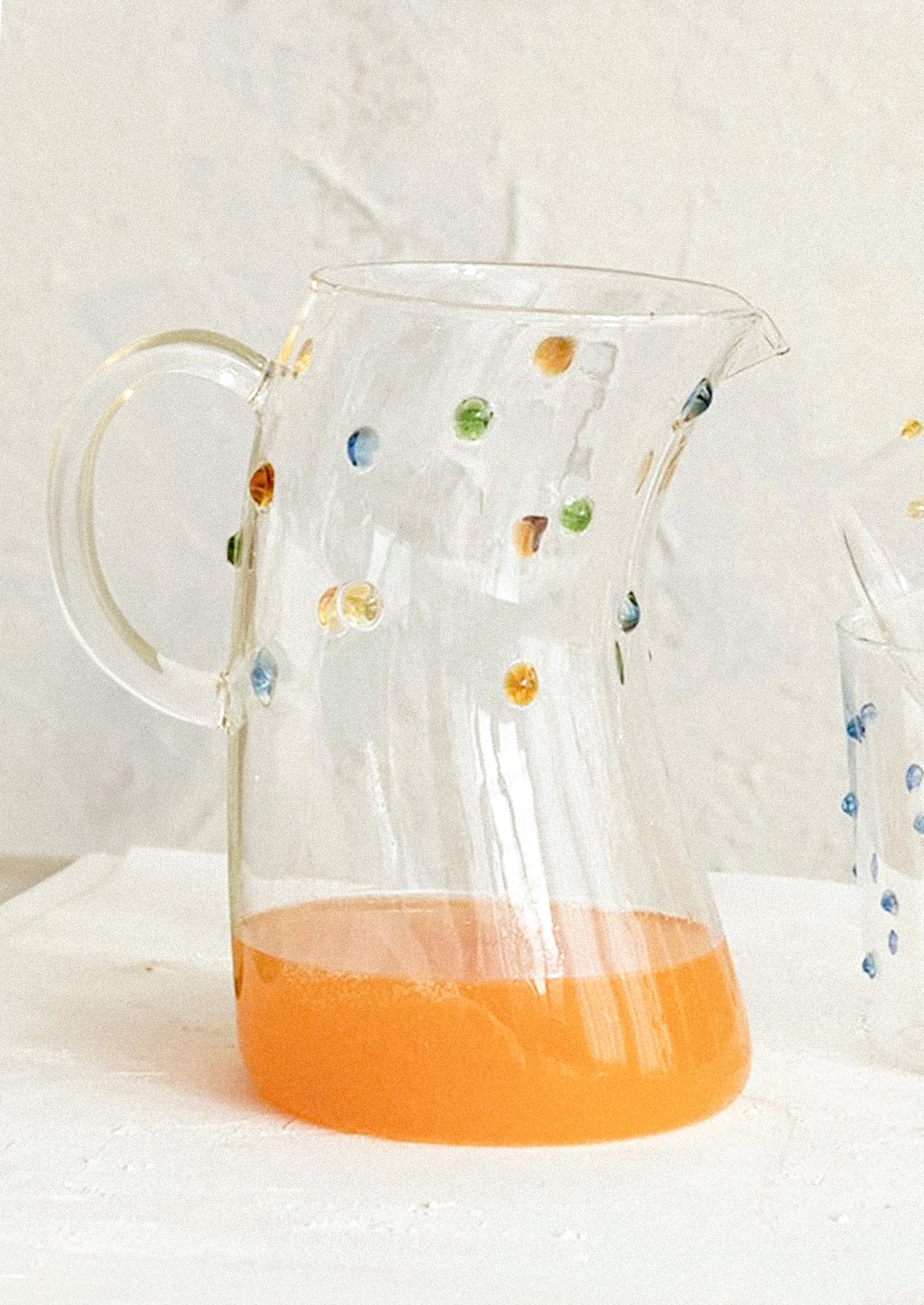 A skewed shape clear glass pitcher with colorful dot detail.