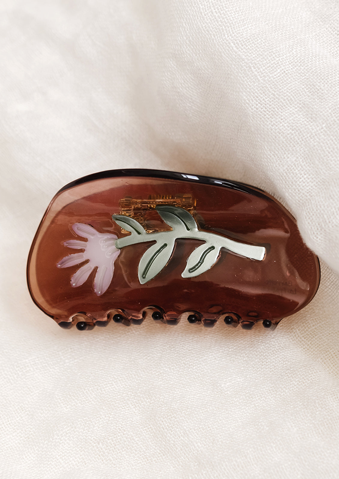 A brown curved shape hair claw with green and purple aster flower.