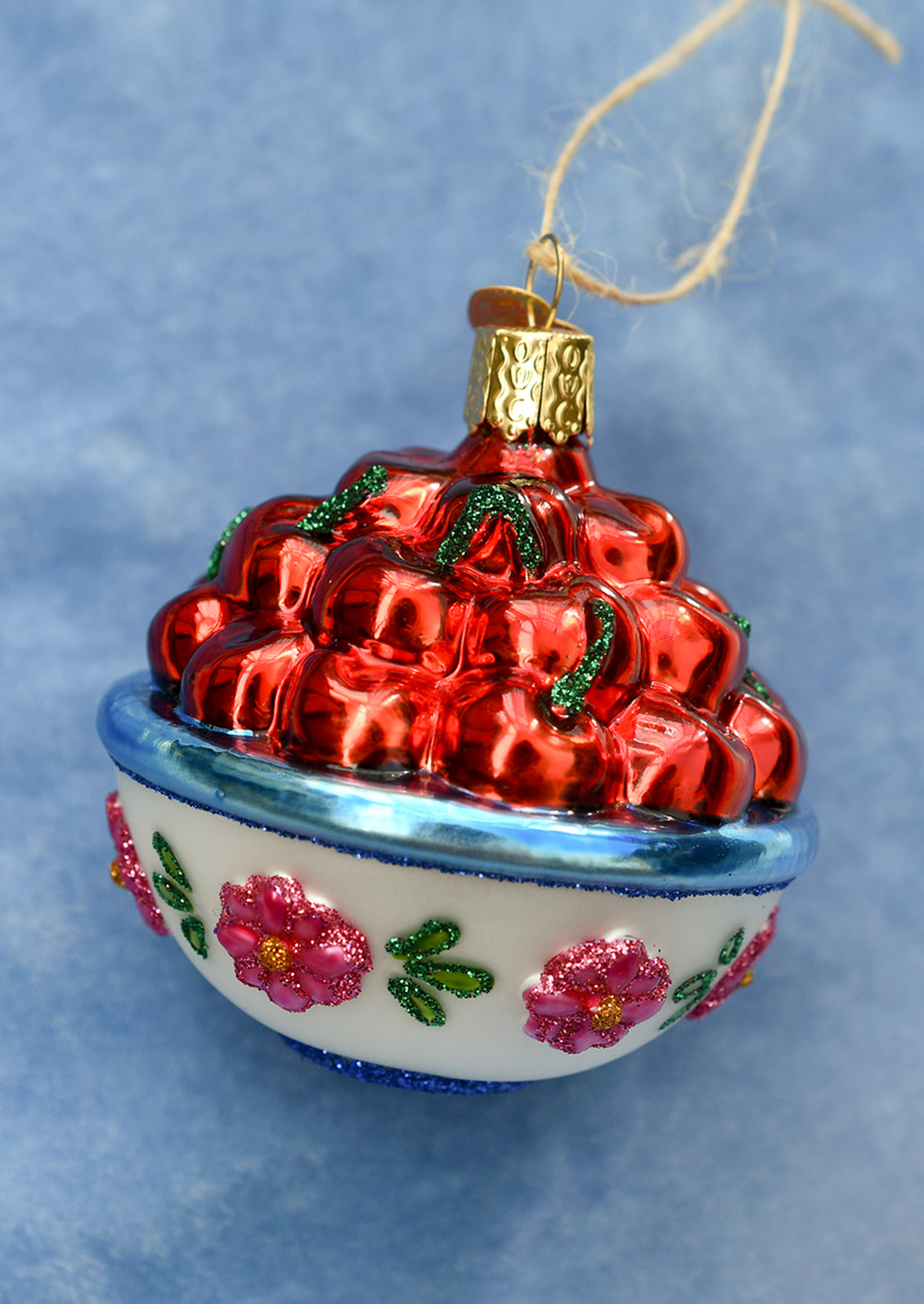 A glass ornament of cherries in a floral print bowl.