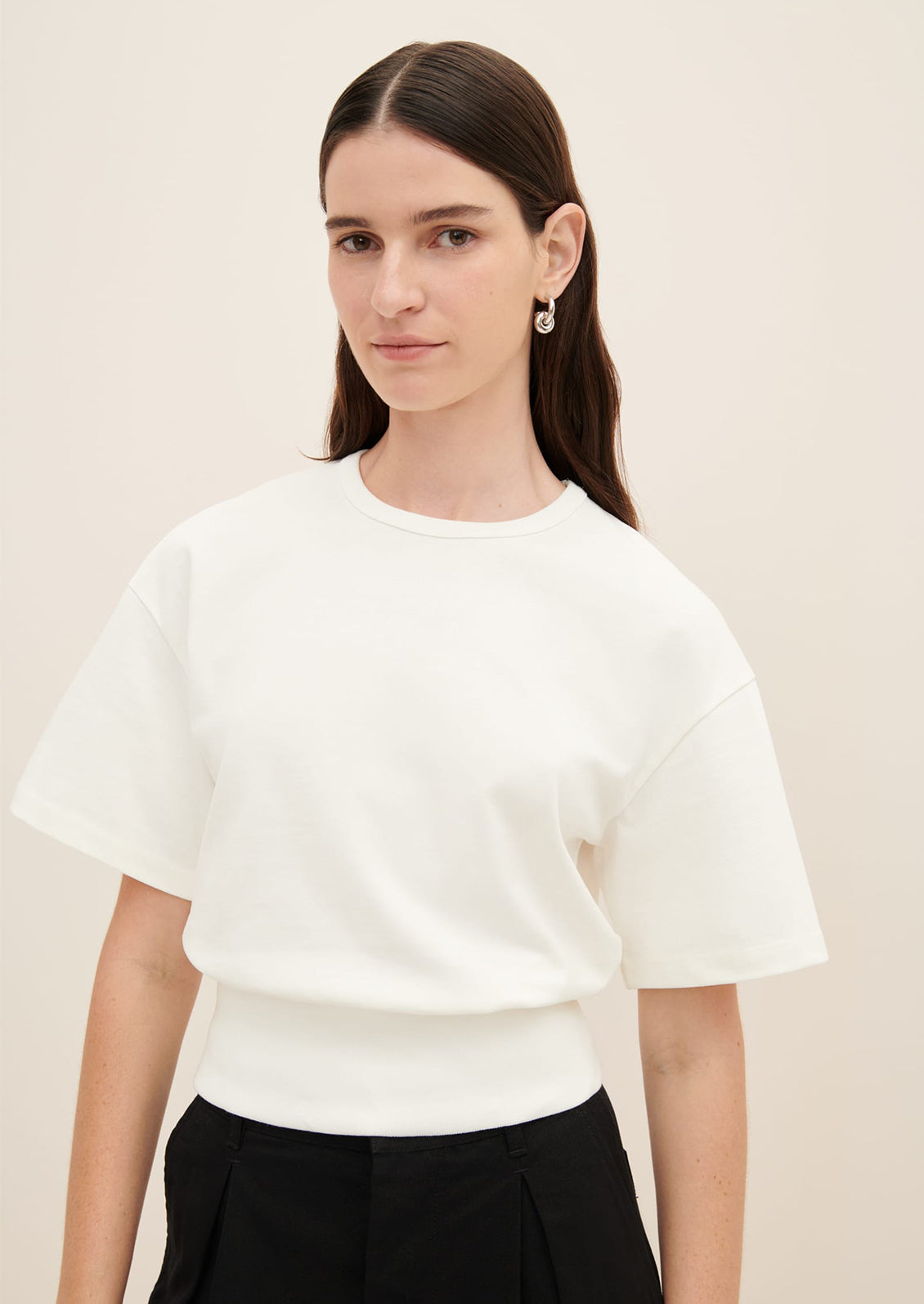 A woman wearing a boxy tee with short sleeves and fitted ribbed waistband, in white.