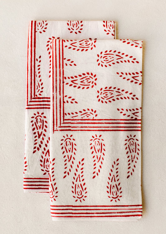 A pair of white cotton napkins with block printed paisley pattern in red.