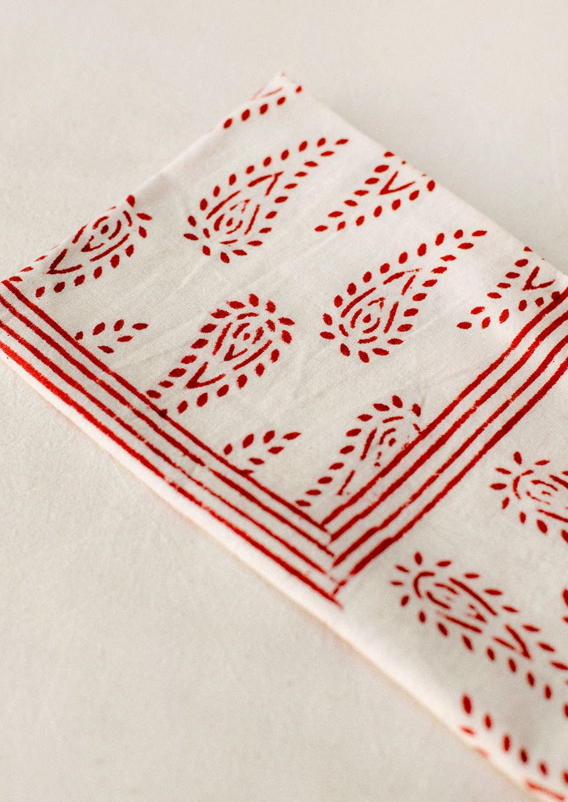 A pair of white cotton napkins with block printed paisley pattern in red.