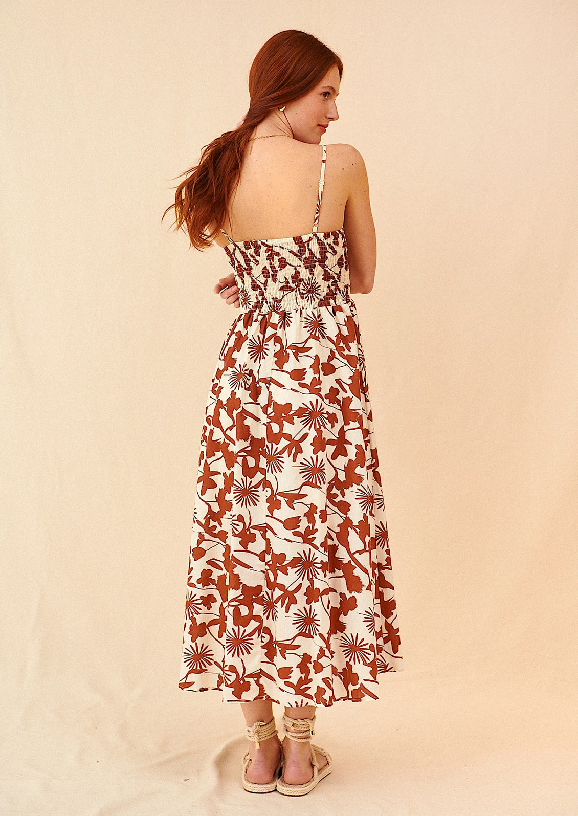 A woman wearing a sleeveless spaghetti strap dress in brown and white botanical print.