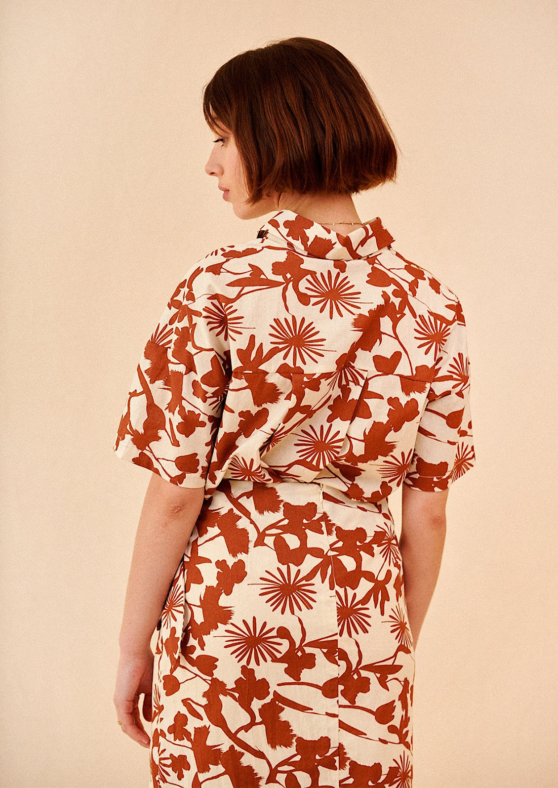 A woman wearing a short sleeve safari-style shirt in brown and white botanical print.