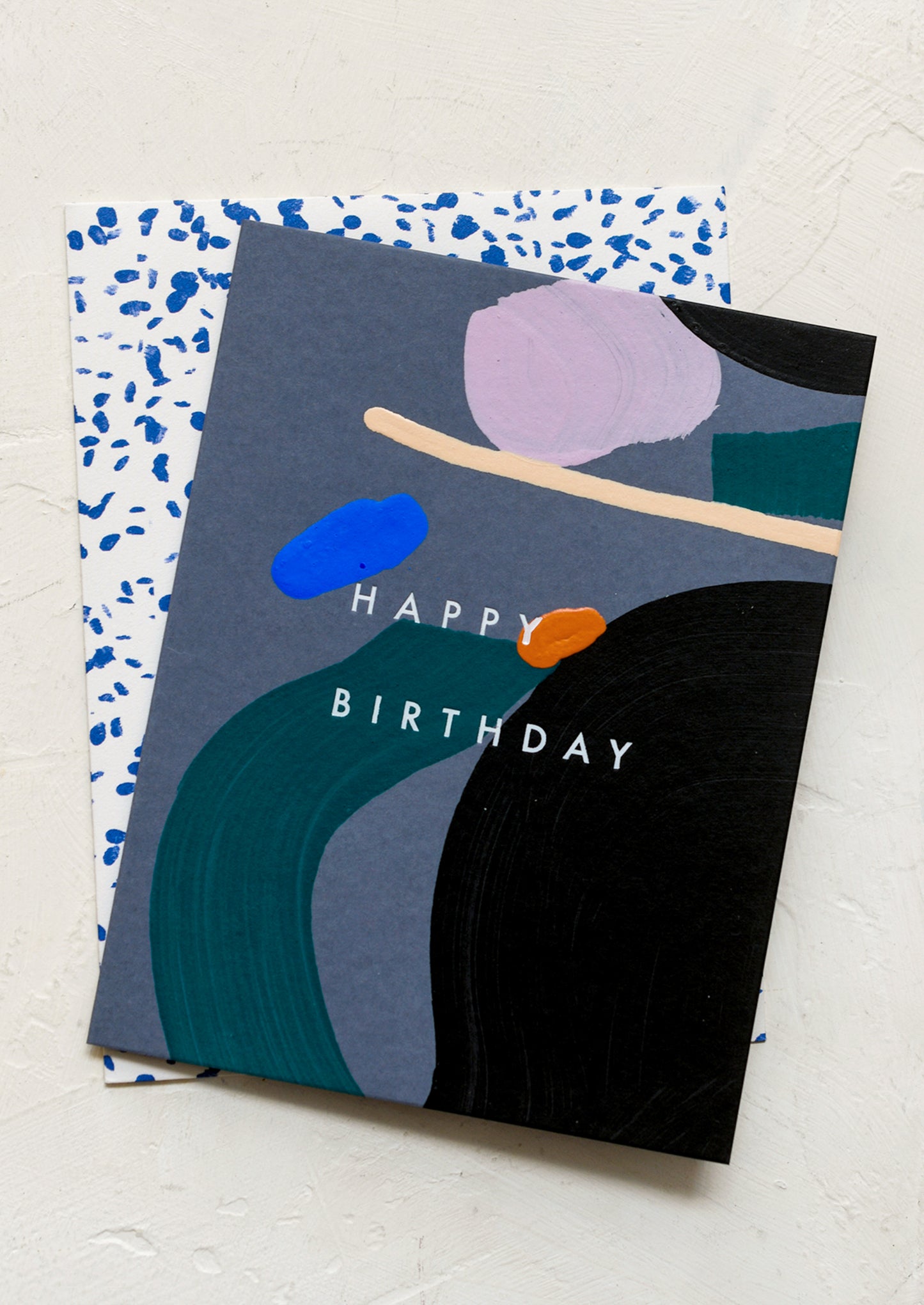 A greeting card in grey with dark abstract paint decoration, reads "Happy Birthday" on front.