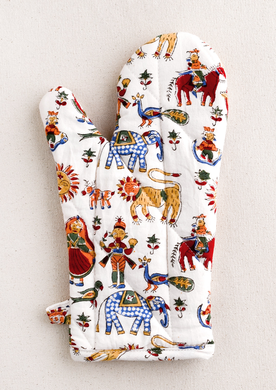 A quilted cotton oven mitt with multicolor, carnival-themed block printed pattern.