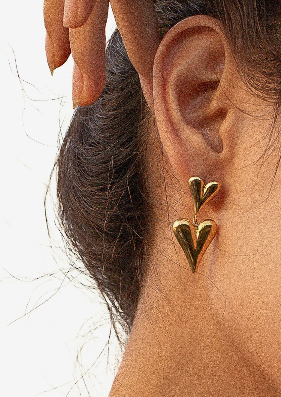 A pair of gold earrings with small heart on top of big heart.