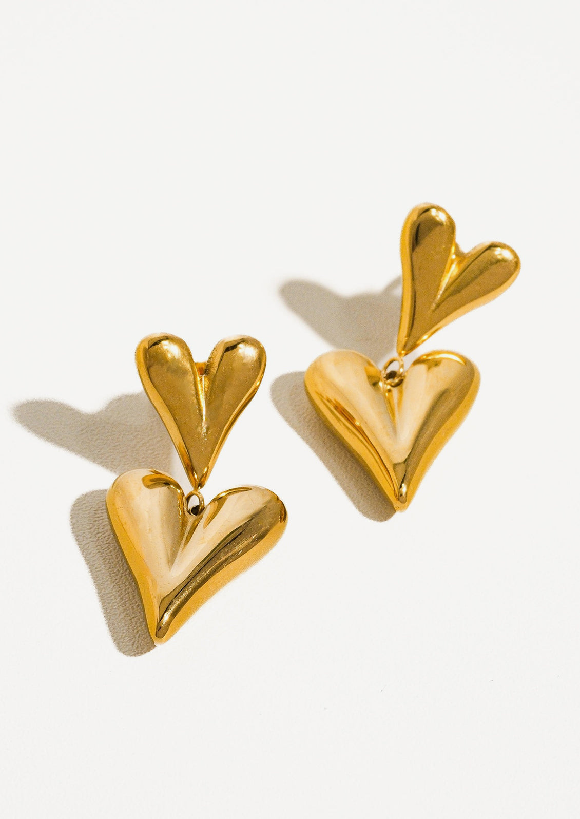 A pair of gold earrings with small heart on top of big heart.