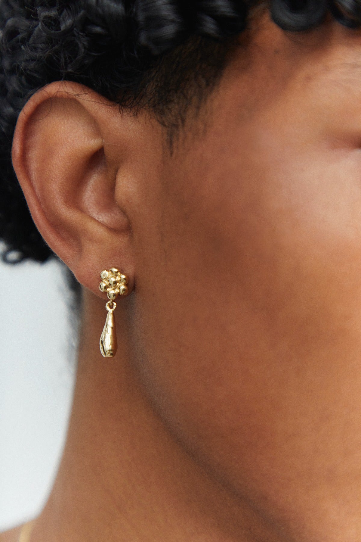 A pair of gold earrings with flower post and teardrop charm.