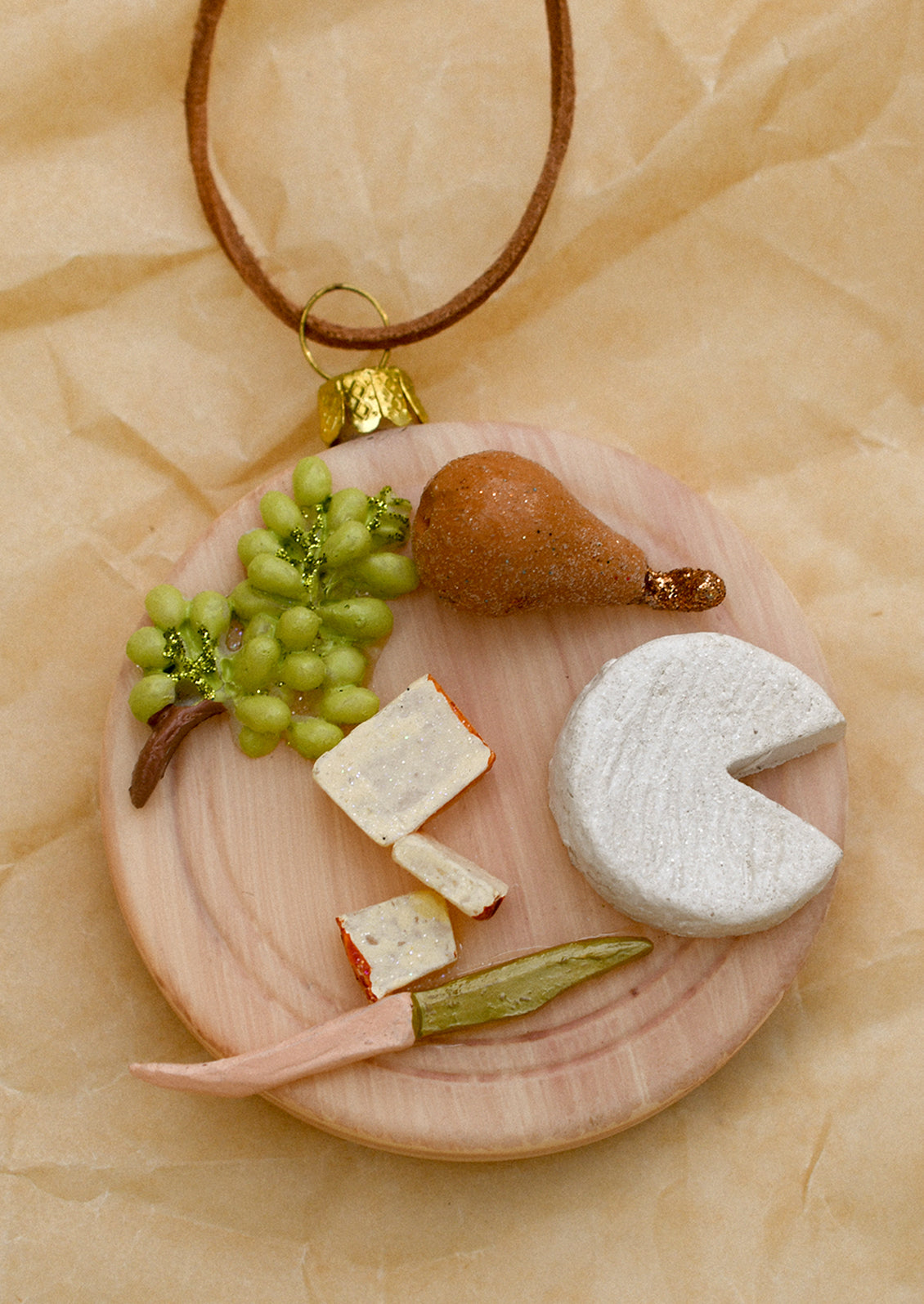 A glass ornament of a round board with cheese, fruit and knife.