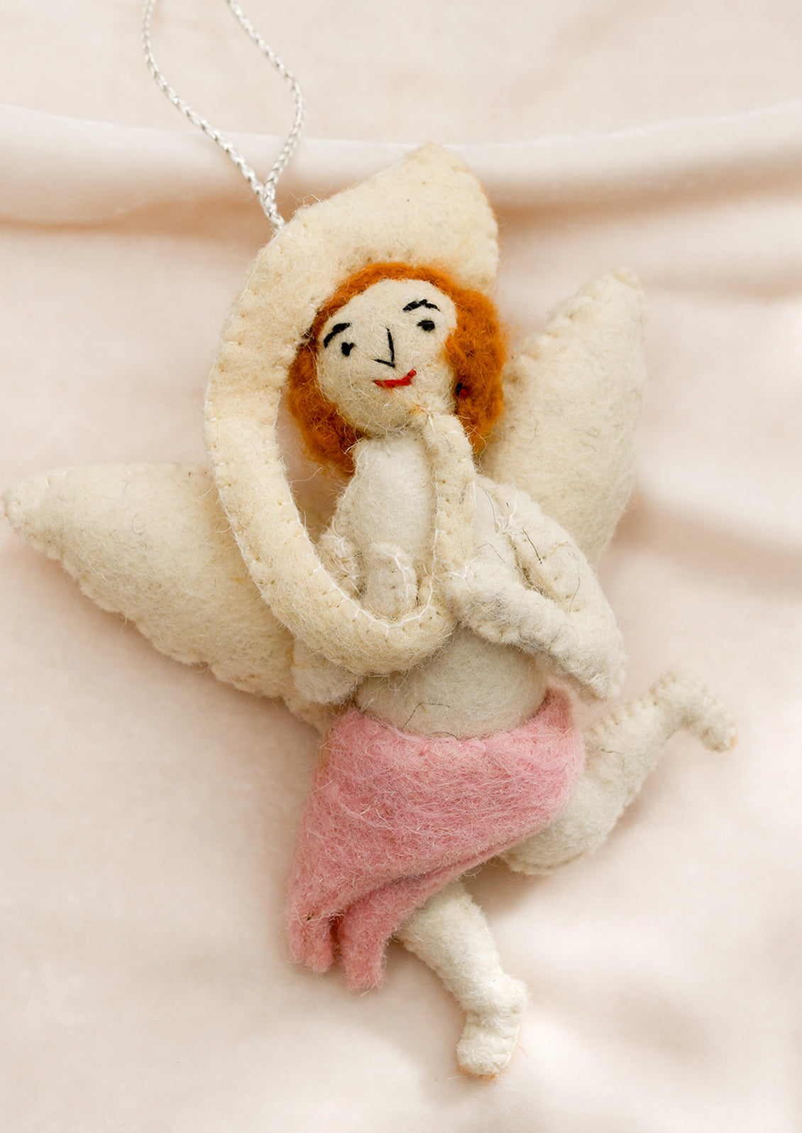 A felt ornament of a cherub wearing pink skirt, holding musical instrument.