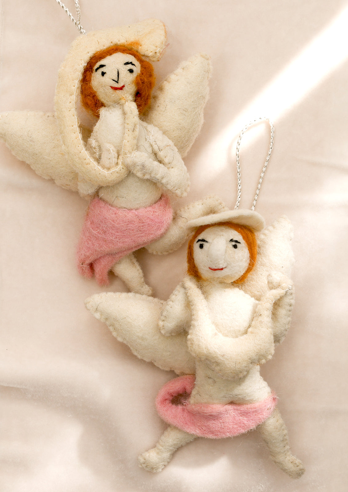 A felt ornament of a cherub wearing pink skirt, holding musical instrument.