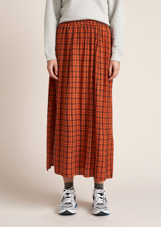 A woman wearing a red-orange skirt with navy tartan check pattern.