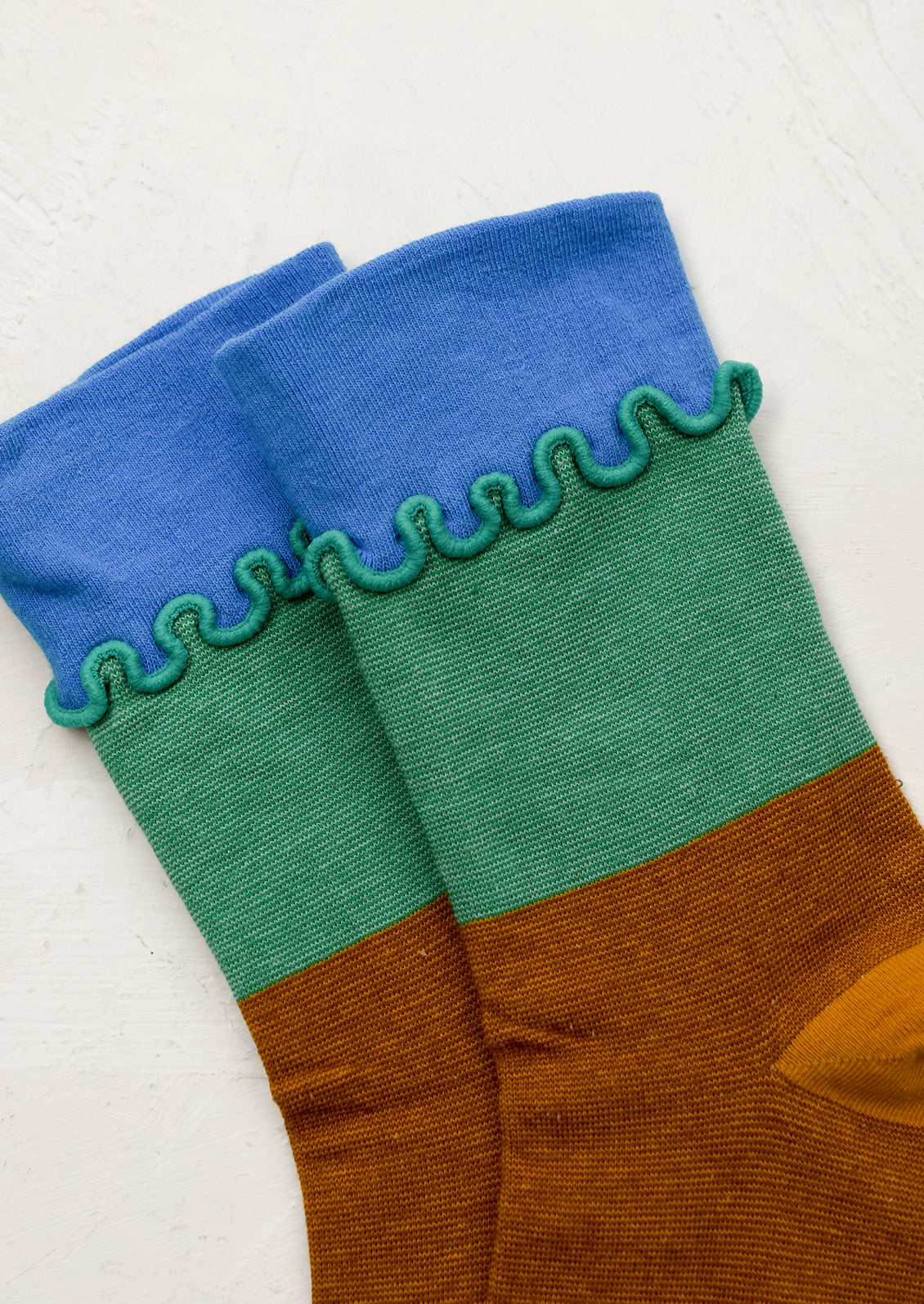 A pair of multicolor color blocked socks with squiggly ruffle trim at ankle.