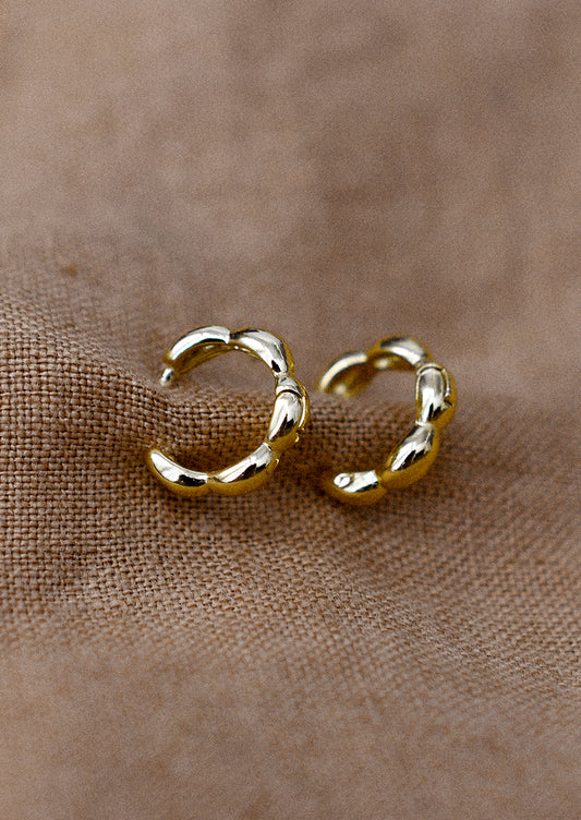 A pair of small gold huggie hoop earrings with scallop shape.