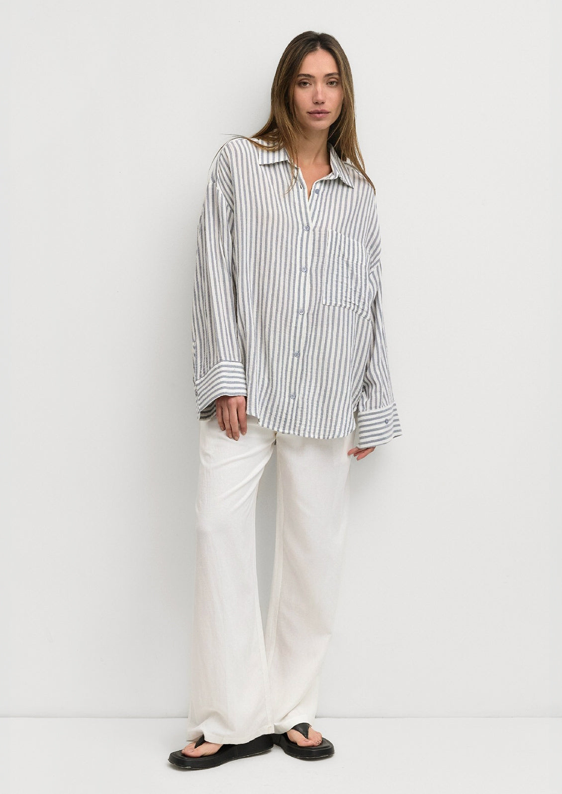 A woman wearing a white and blue stripe cotton gauze button down shirt.