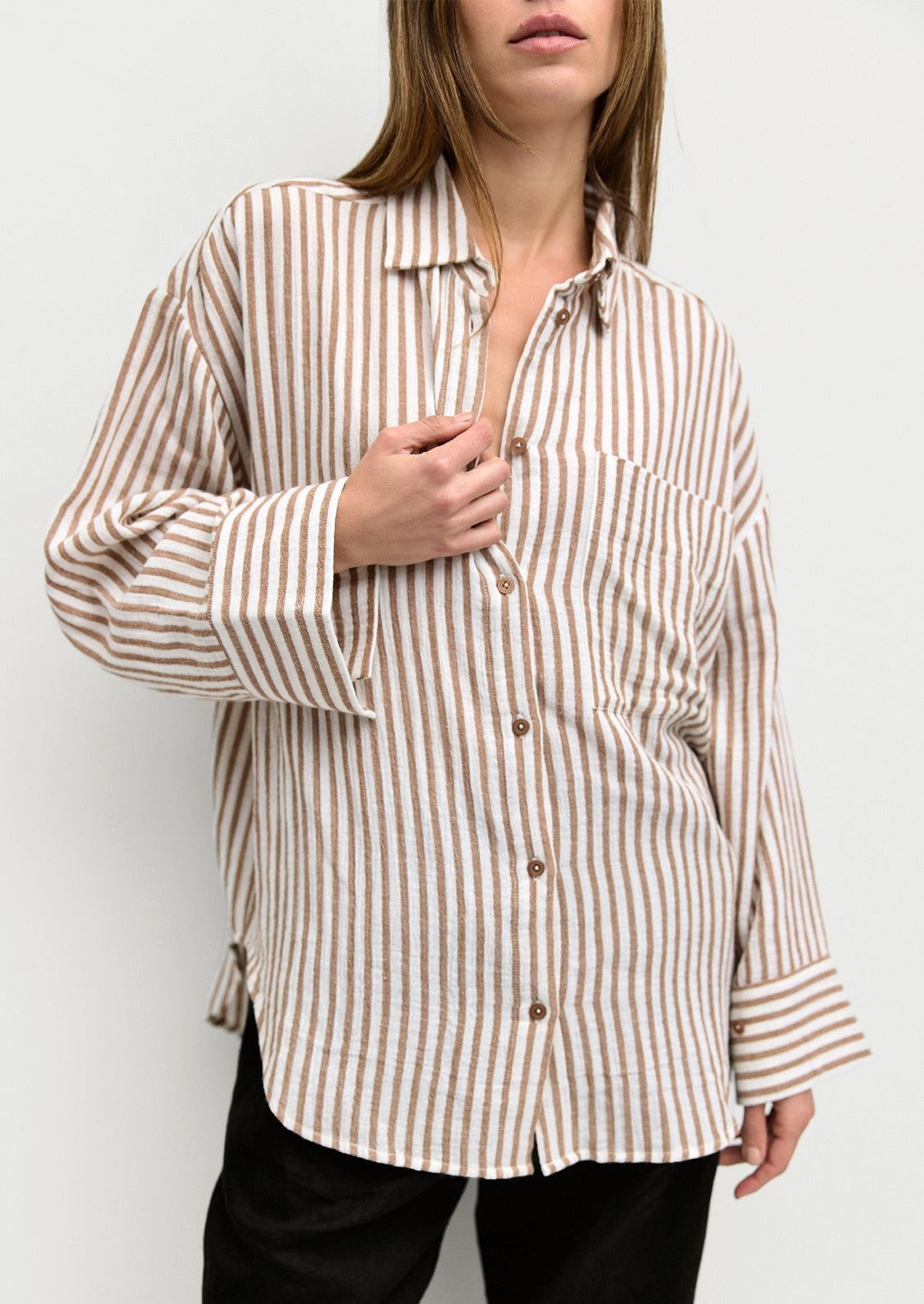 A woman wearing a white and brown stripe cotton gauze button down shirt.