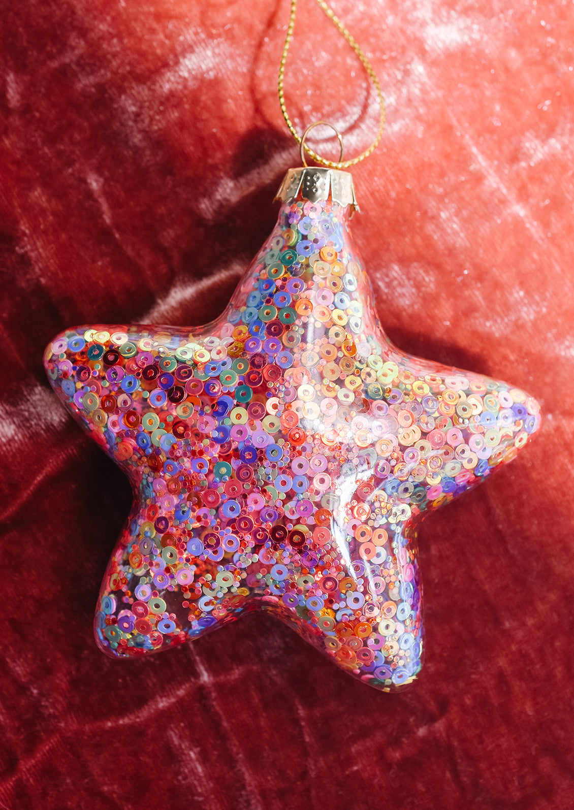 A clear glass star shaped ornament with multicolor sequins inside.