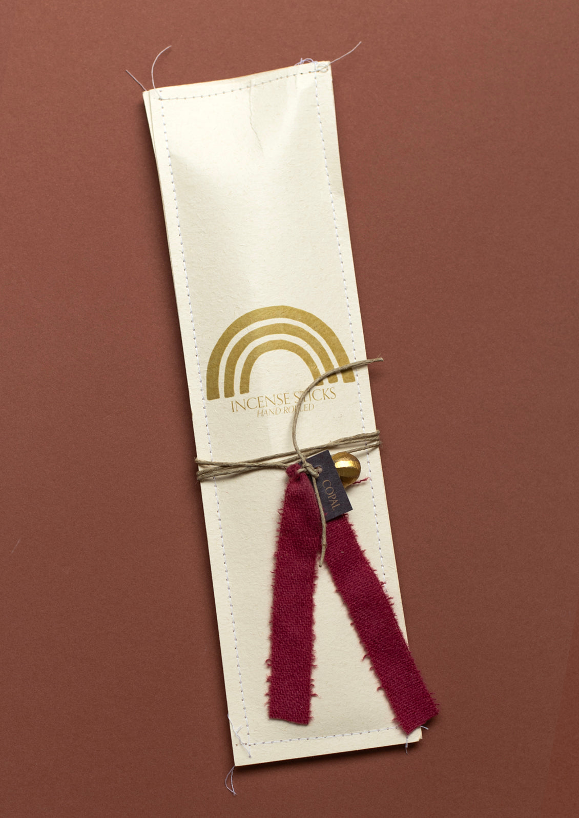 A pack of incense with burgundy silk ribbon and brass charm, in copal scent.