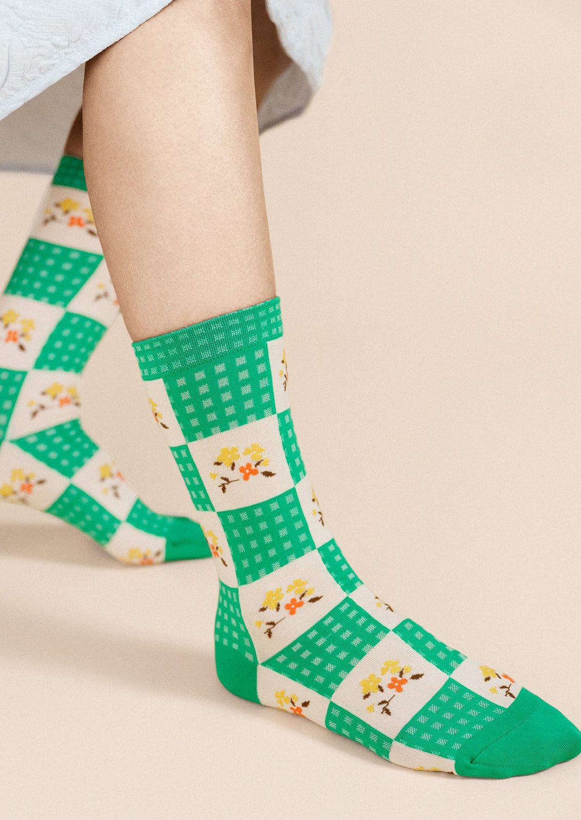 A woman wearing a pair of socks in green and cream gingham with yellow floral pattern.