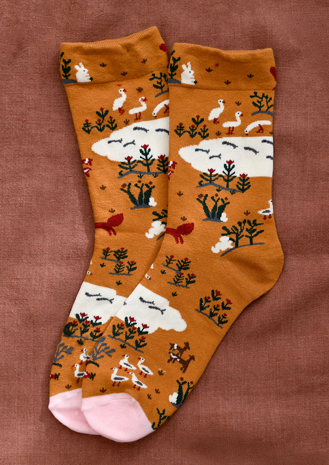 A pair of caramel colored socks with whimsical animal and nature print in white, red and green.