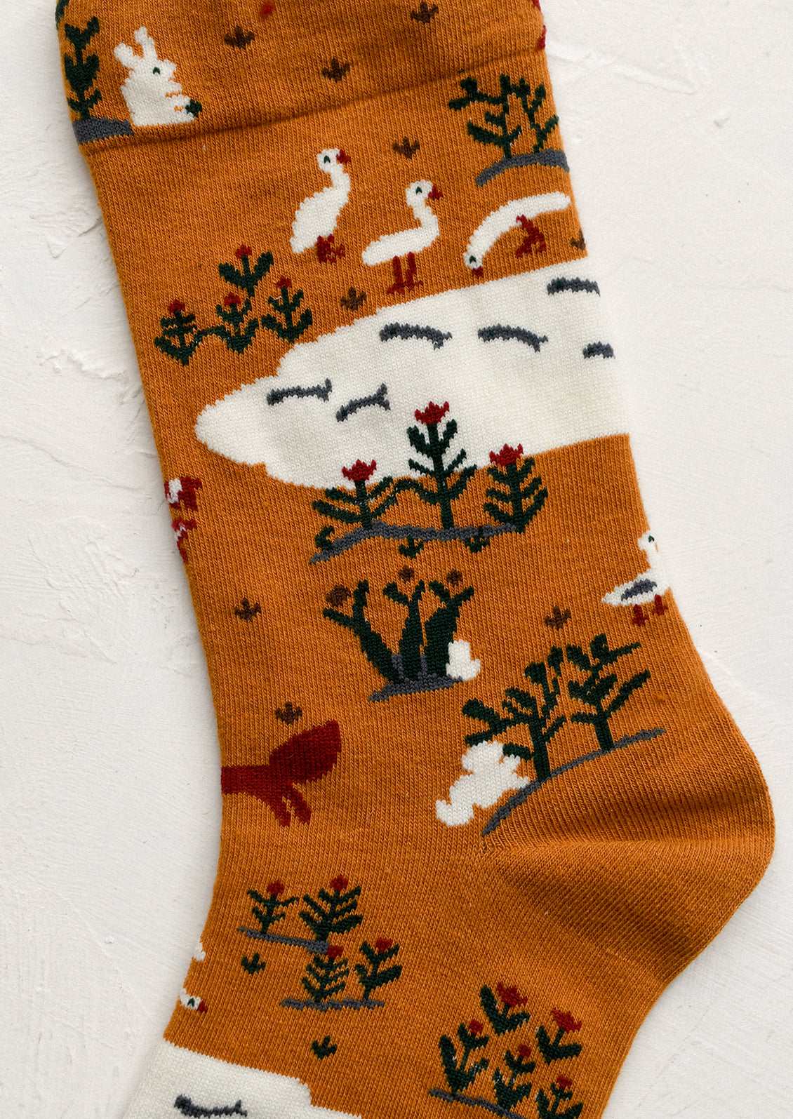 A pair of caramel colored socks with whimsical animal and nature print in white, red and green.