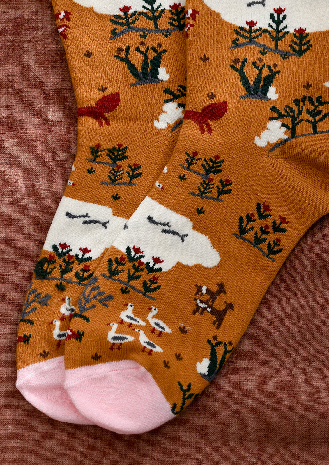 A pair of caramel colored socks with whimsical animal and nature print in white, red and green.