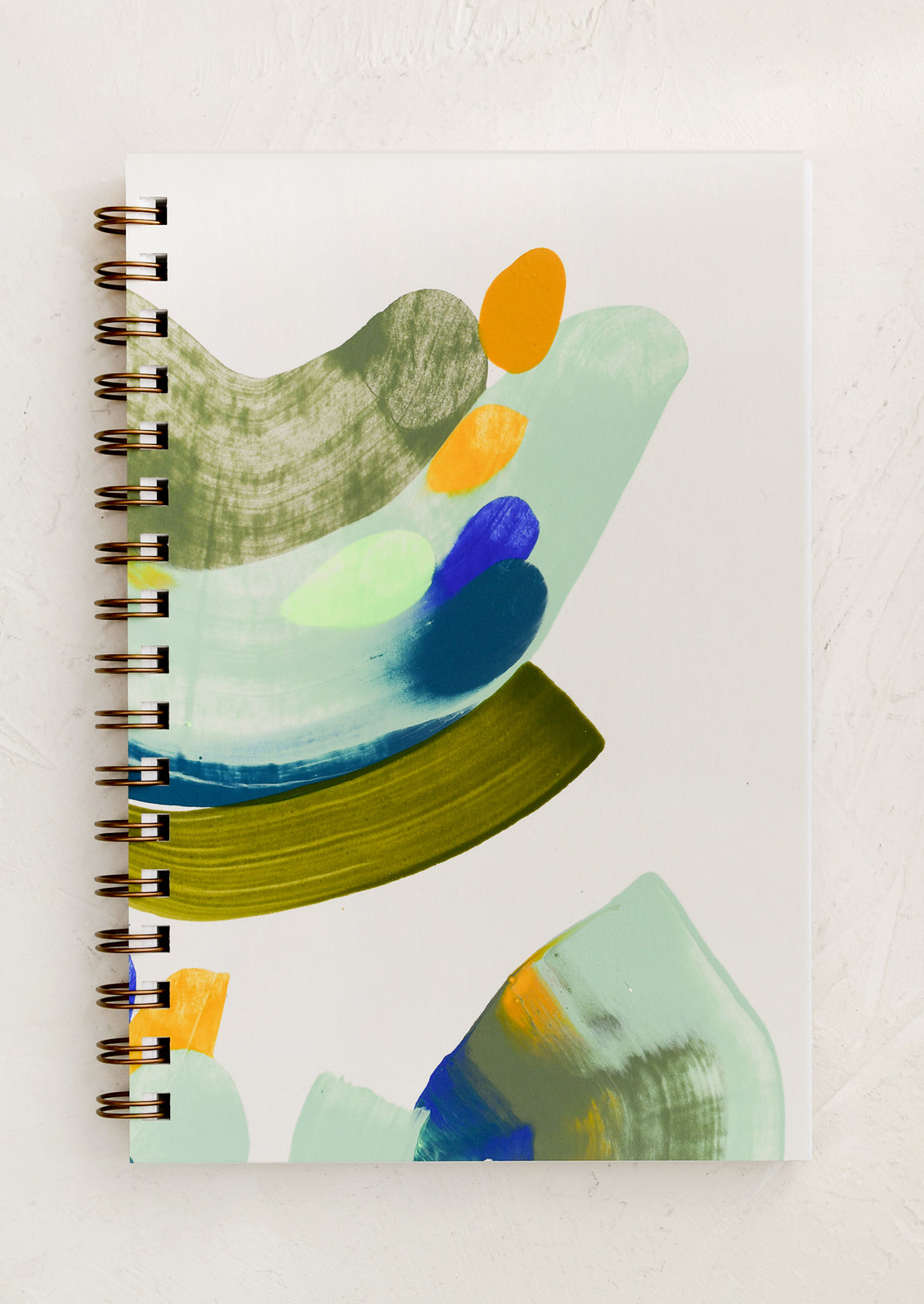 A spiral bound notebook painted with abstract pattern in green and blue.