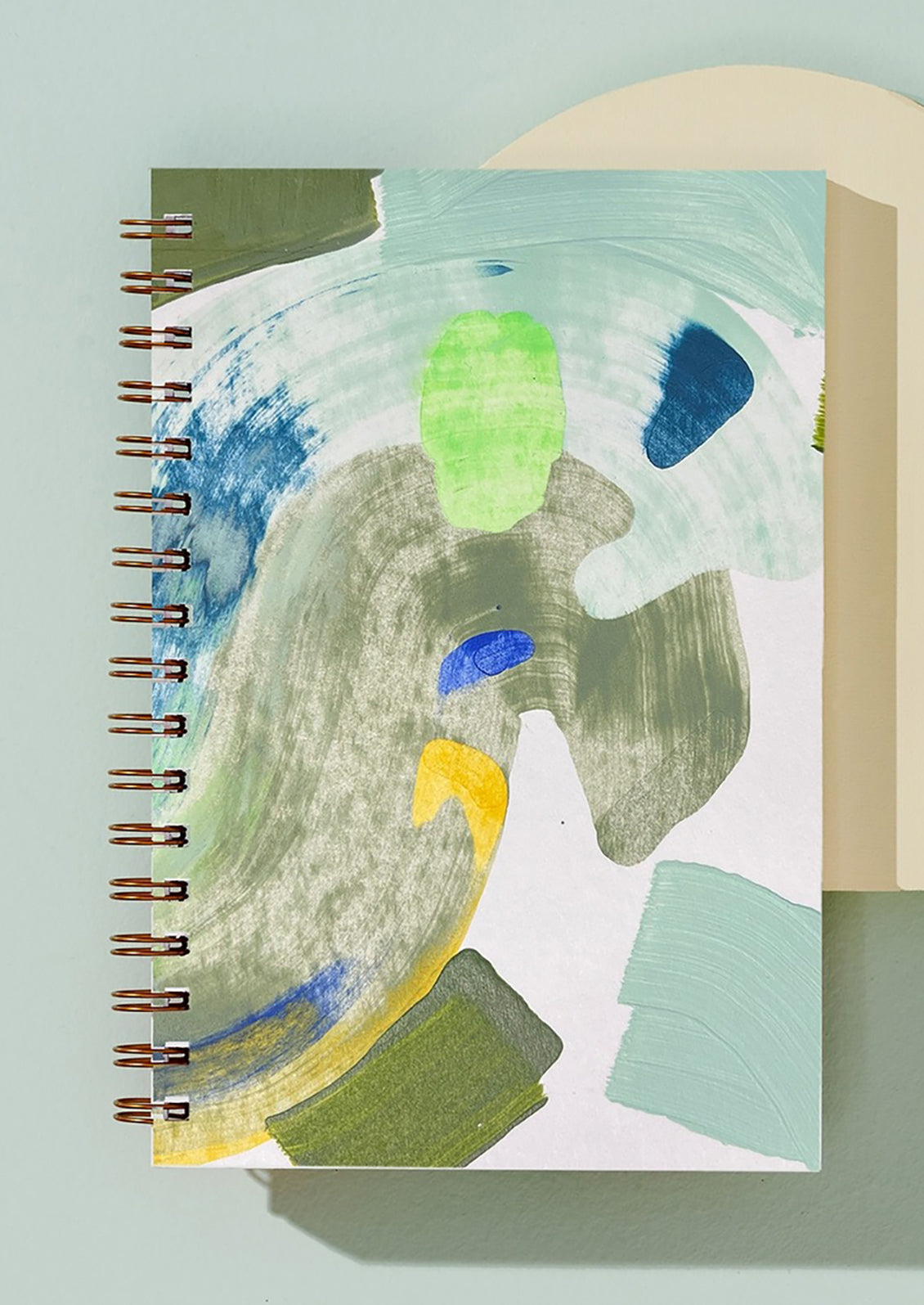 A spiral bound notebook painted with abstract pattern in green and blue.