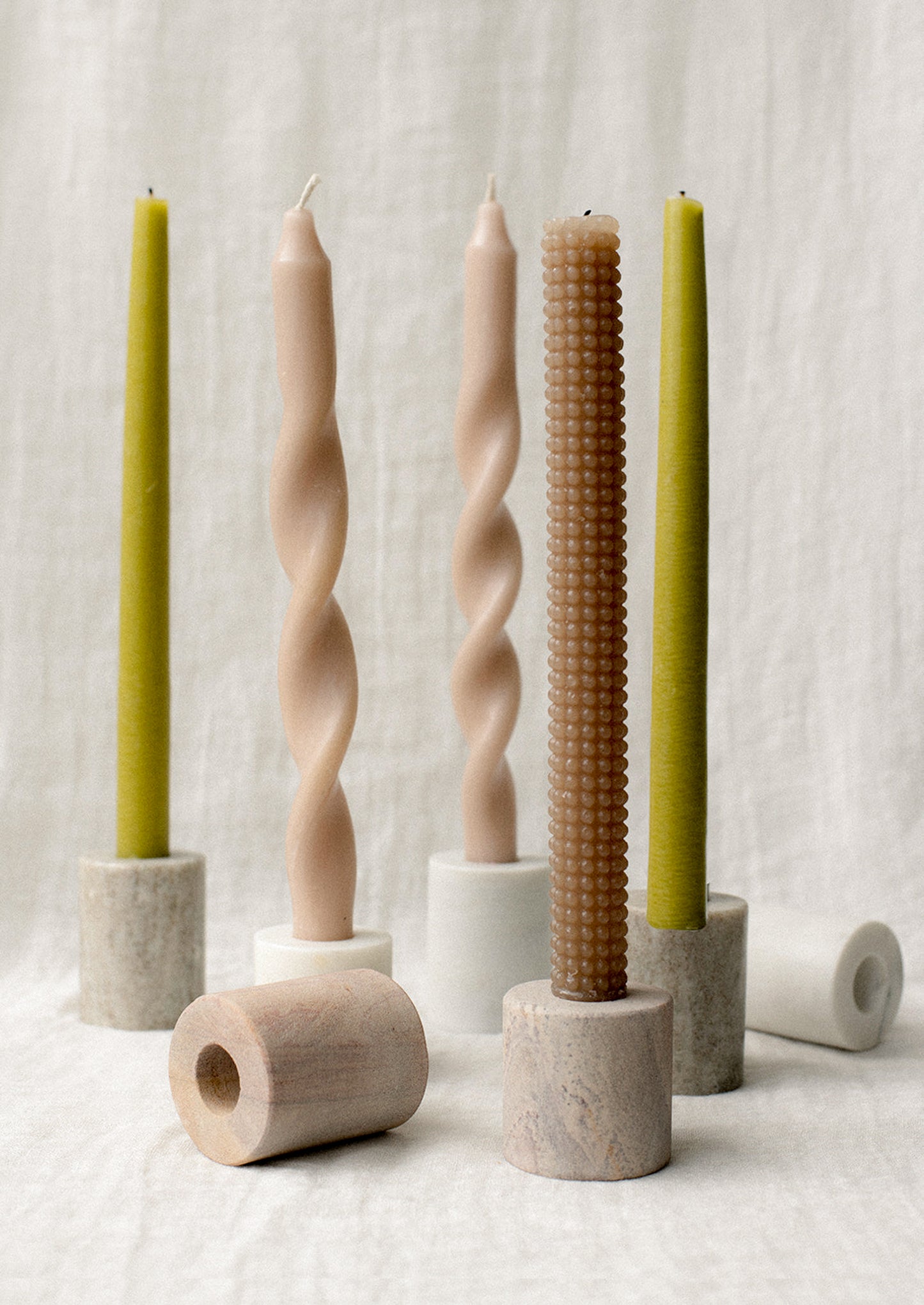 Assorted cylindrical candleholders in tones of white and beige marble.