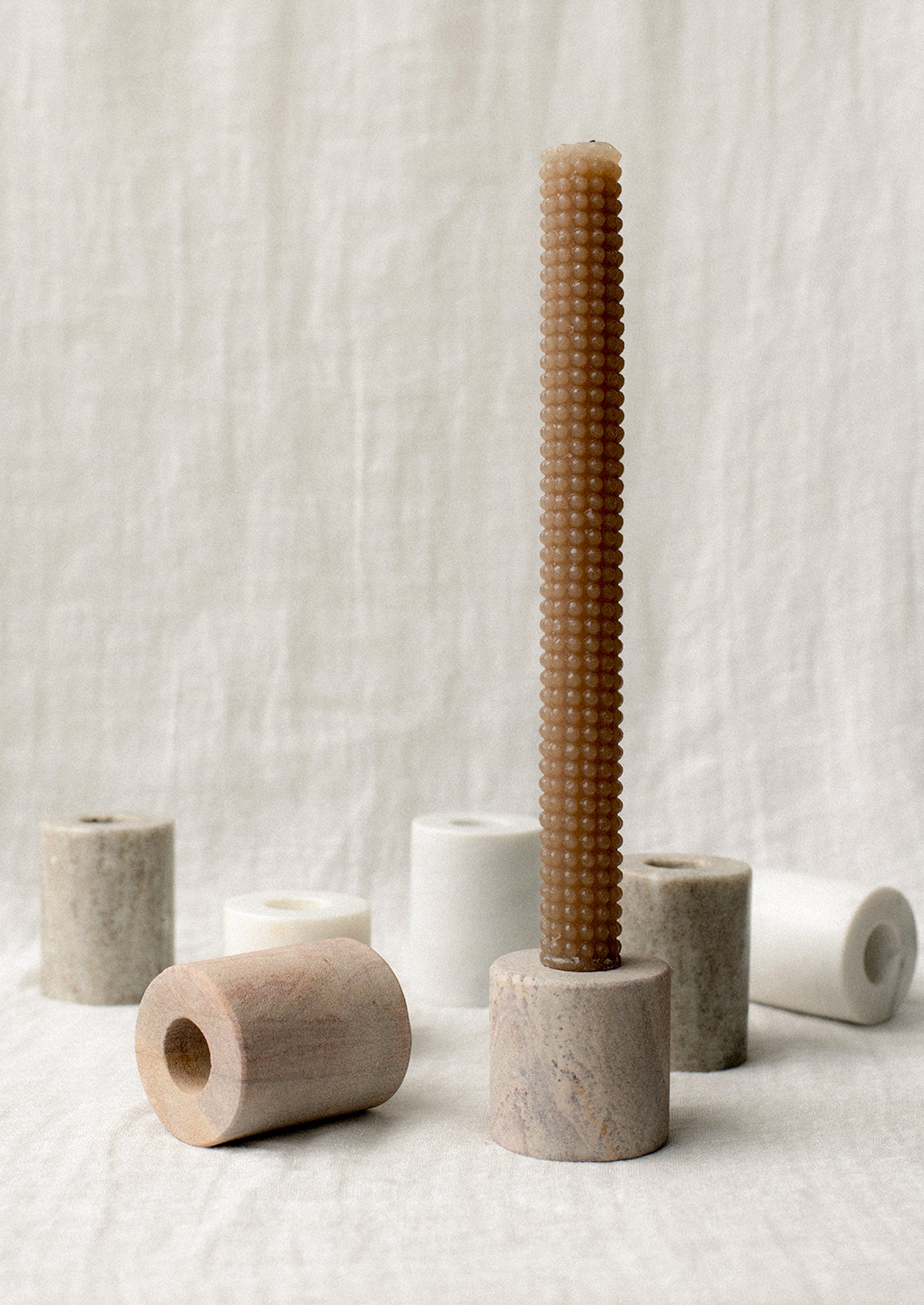 Assorted cylindrical candleholders in tones of white and beige marble.