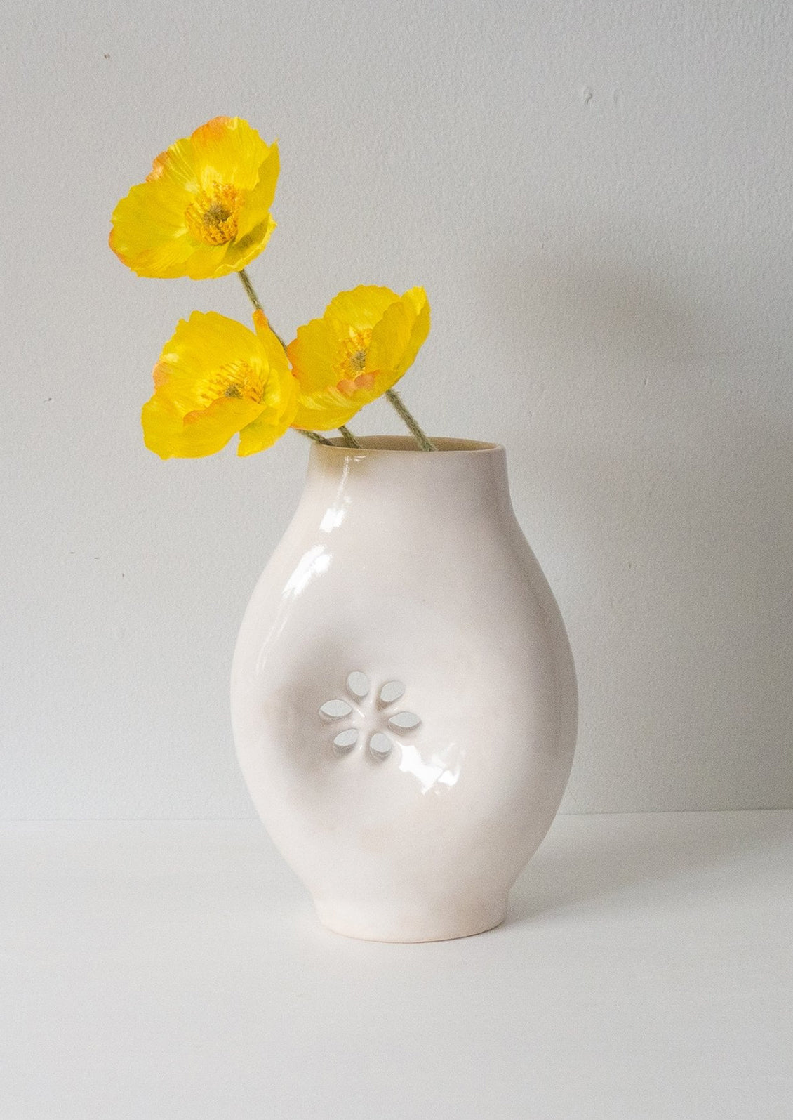 A glossy white ceramic vase with asymmetrical flower cutout detail.