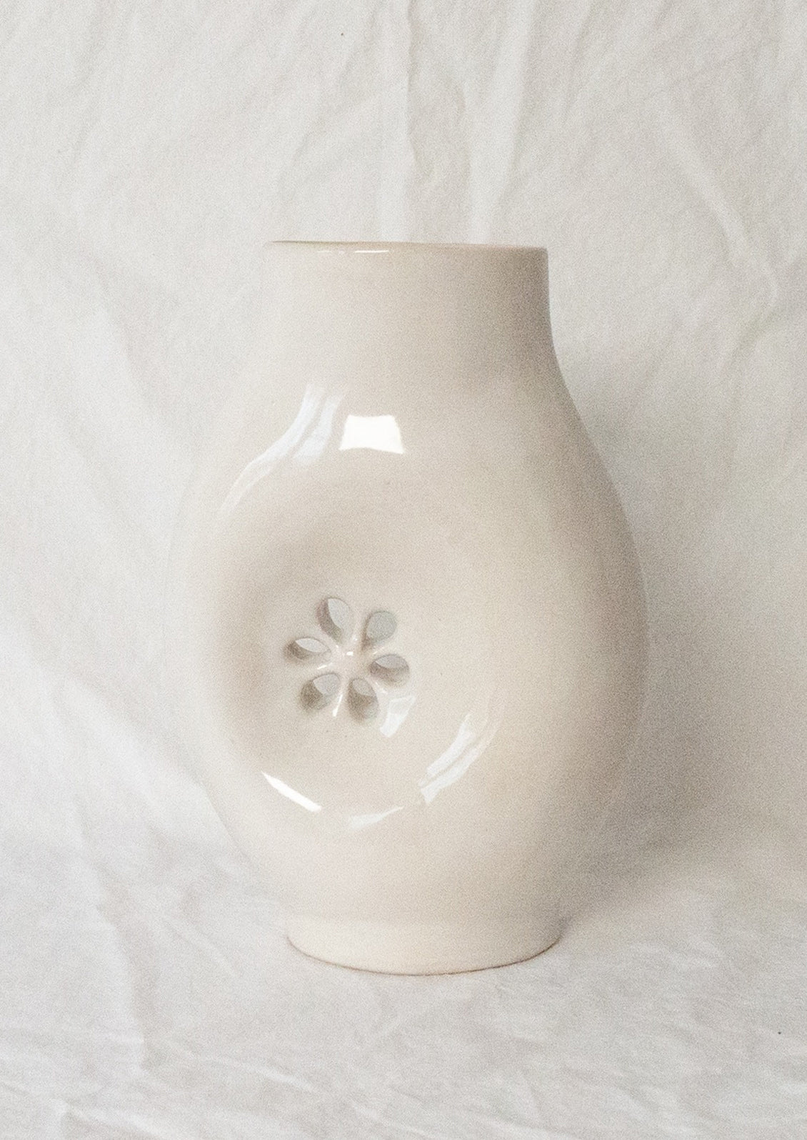 A glossy white ceramic vase with asymmetrical flower cutout detail.