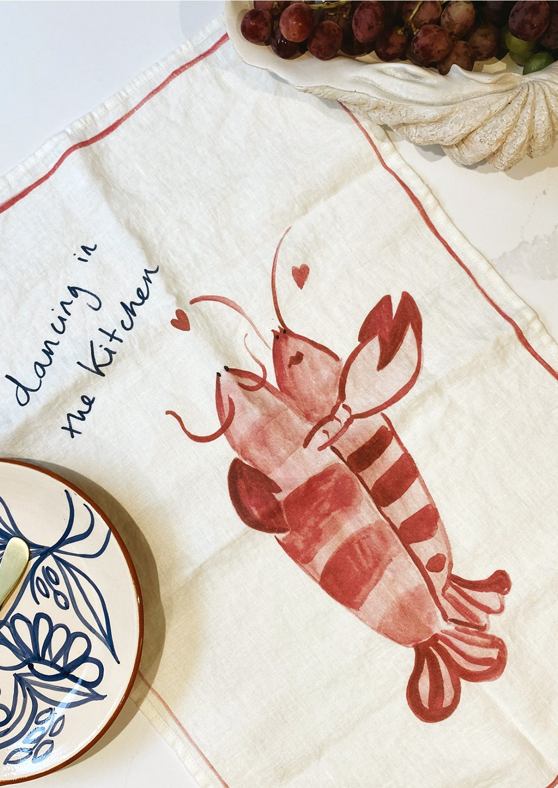 A white linen tea towel with lobster graphic and text.