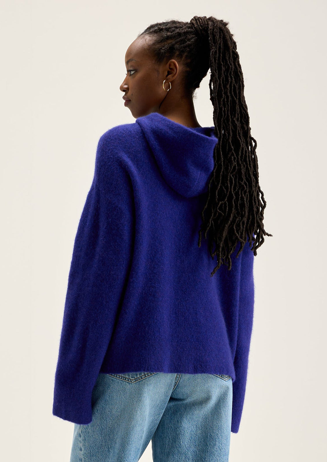 A woman wearing a hooded sweater with kangaroo pocket in vibrant cobalt blue color.