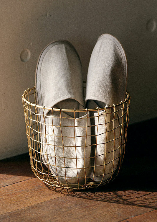 A round brass wire storage basket holding one pair of slippers.