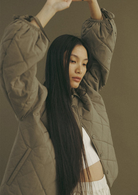 A woman wearing a quilted, padded jacket in army green with tie detail at wrists.